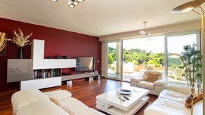 Una sala de estar moderna con una pared de acento roja, muebles blancos y un amplio ventanal corredera que da a un patio exterior.