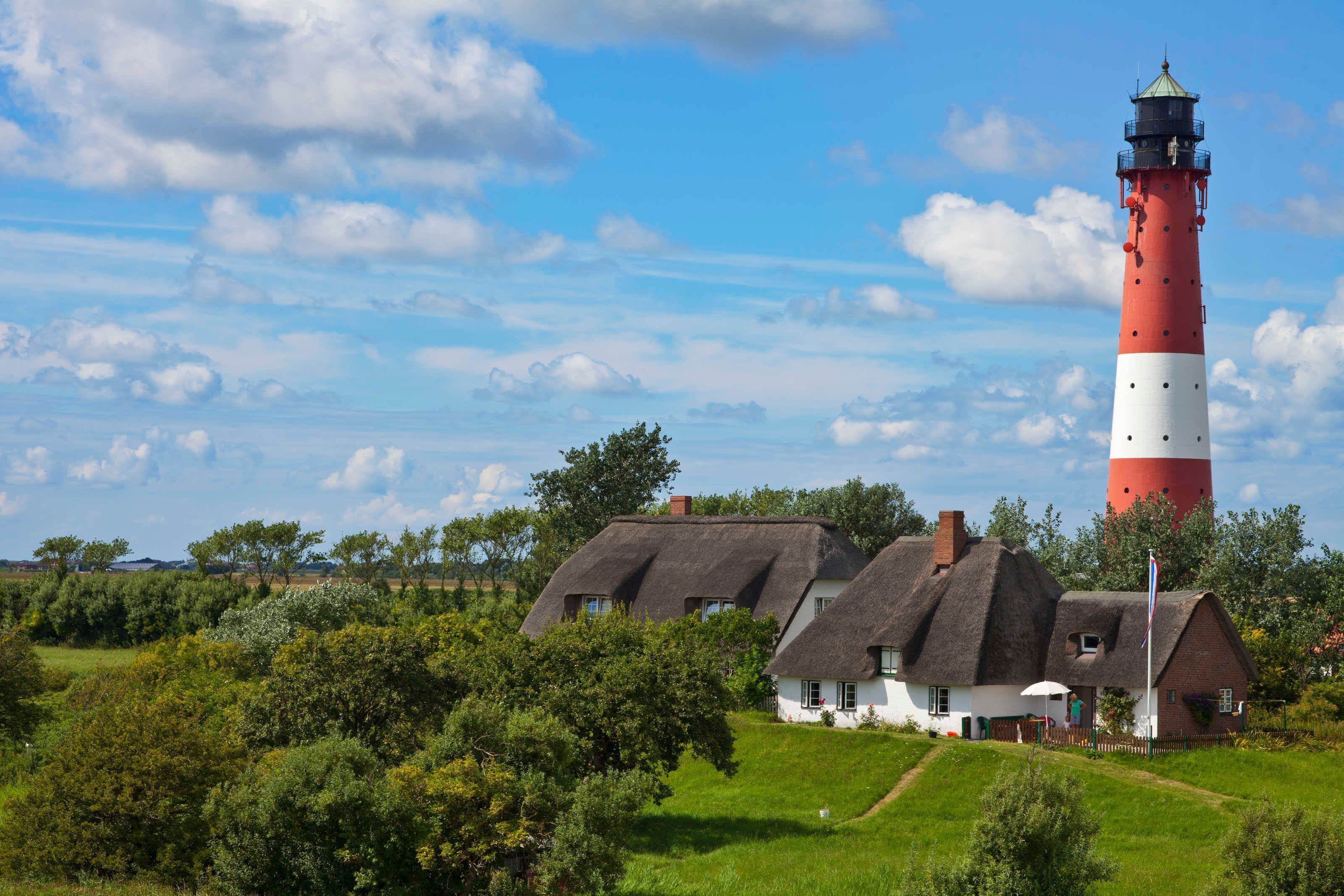 A lighthouse with a red and white tower, surrounded by thatched-roof houses and greenery.