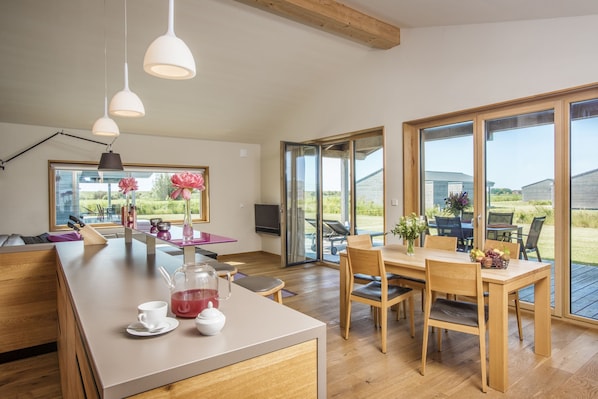 A modern kitchen with a large island, dining area, and large windows offering a view of the outdoors.