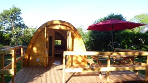 A wooden arched structure with a wooden deck and picnic table, surrounded by greenery.