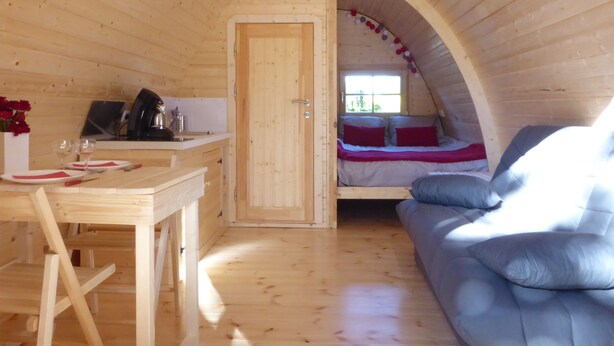 A cozy loft bedroom with a wooden ceiling, a small kitchenette, and a sofa.