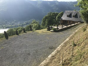 Un bâtiment doté d’un toit en pente, d’une allée gravillonnée et offrant une vue sur une vallée parsemée d’arbres et comprenant une étendue d’eau.