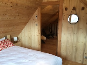 Une pièce en bois avec un lit, une petite table et un miroir au mur.