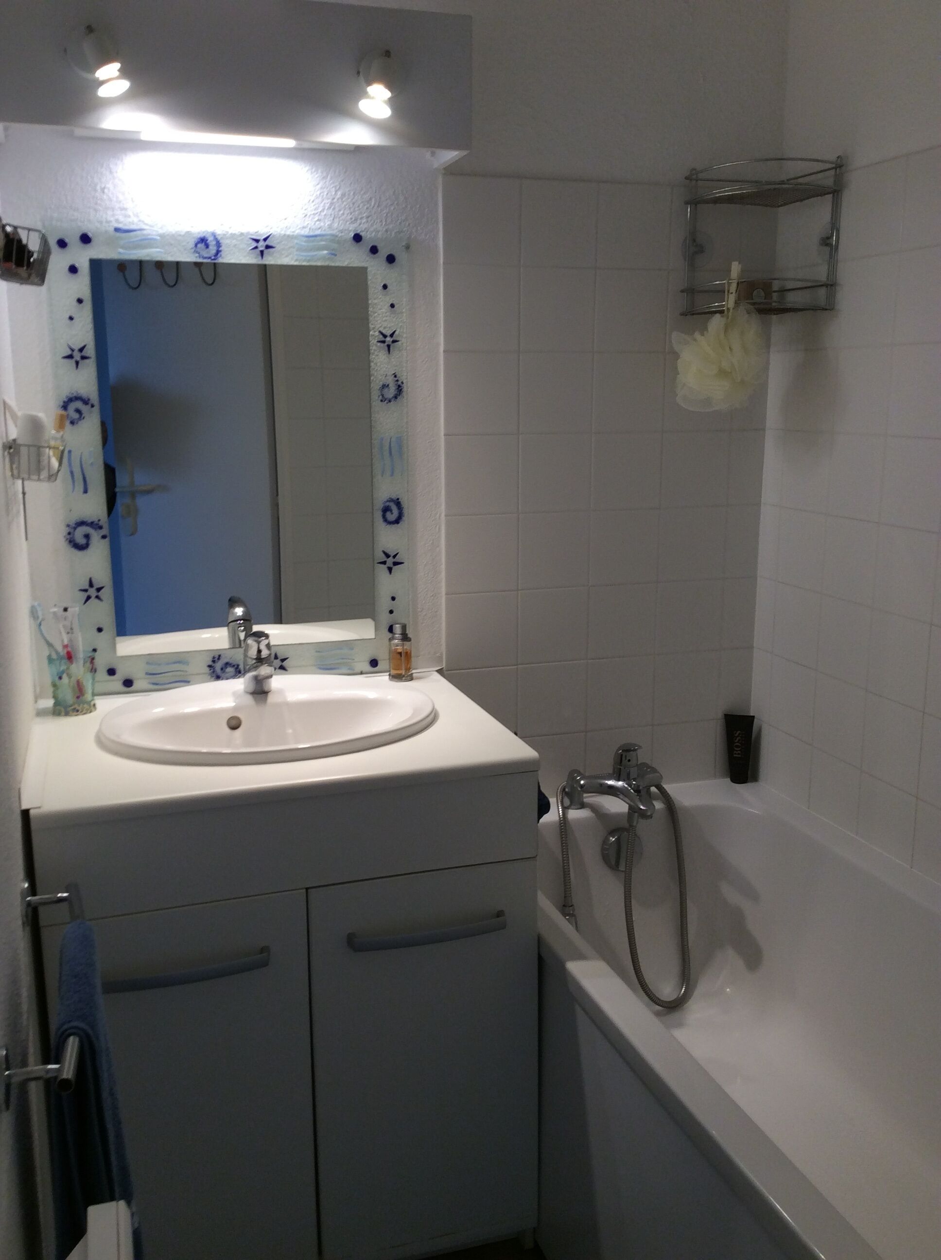 A bathroom with a white sink, mirror, and bathtub. There is a towel rack and a shower caddy on the wall.