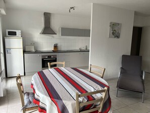 Cozinha compacta com micro-ondas, forno e pia. Há uma mesa de jantar com cadeiras e uma poltrona cinza.