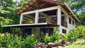 A two-story house with a balcony, surrounded by lush greenery and rocks. - Royal Palm Villas (Cóbano)