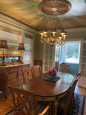 Une salle à manger avec une table en bois, des chaises, un lustre et un plafond décoratif.