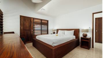 A bedroom with a large bed, wooden furniture, a ceiling fan, and a view through the window blinds.