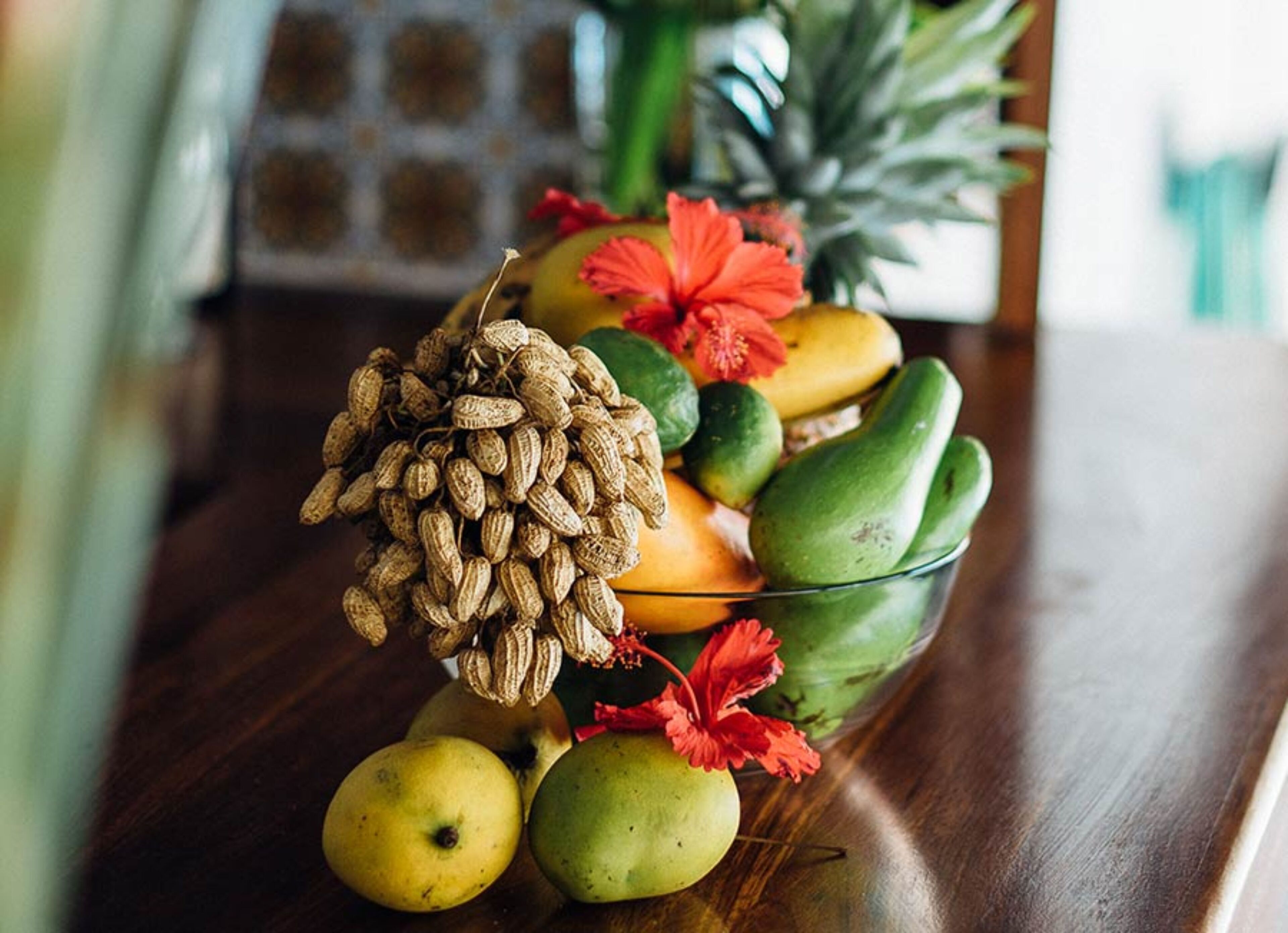 A fruit bowl with various fruits and a pine cone on a wooden table.