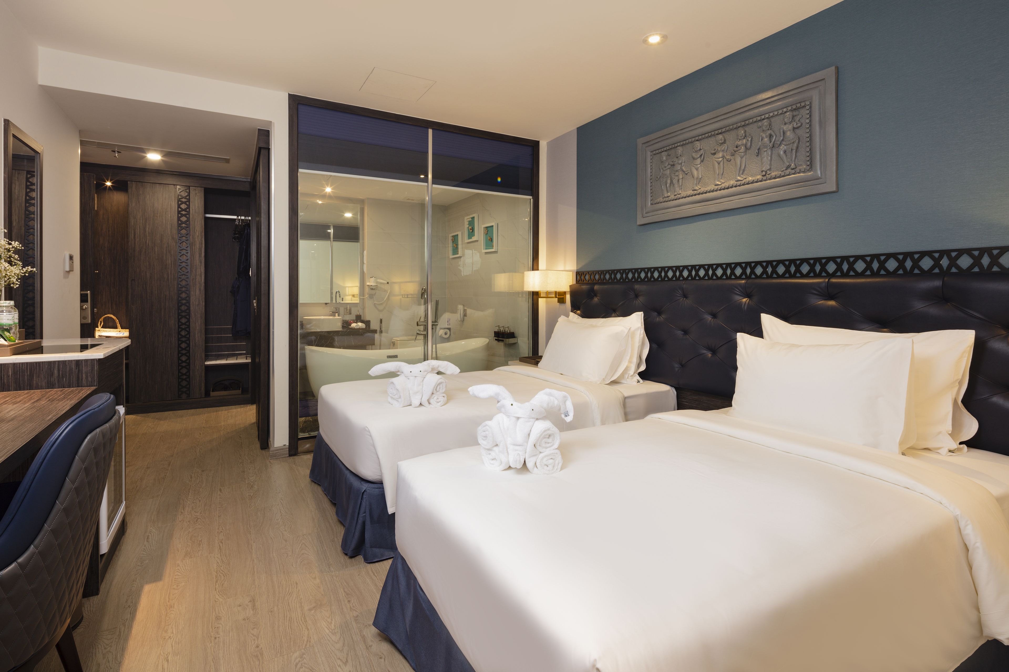 A hotel room with two beds, a dining area, and a bathroom with a glass shower enclosure.