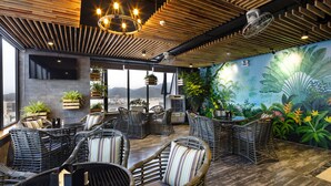A modern lounge area with wicker furniture, a large mural, and a view of the city. - Erica Nha Trang Hotel (Nha Trang)