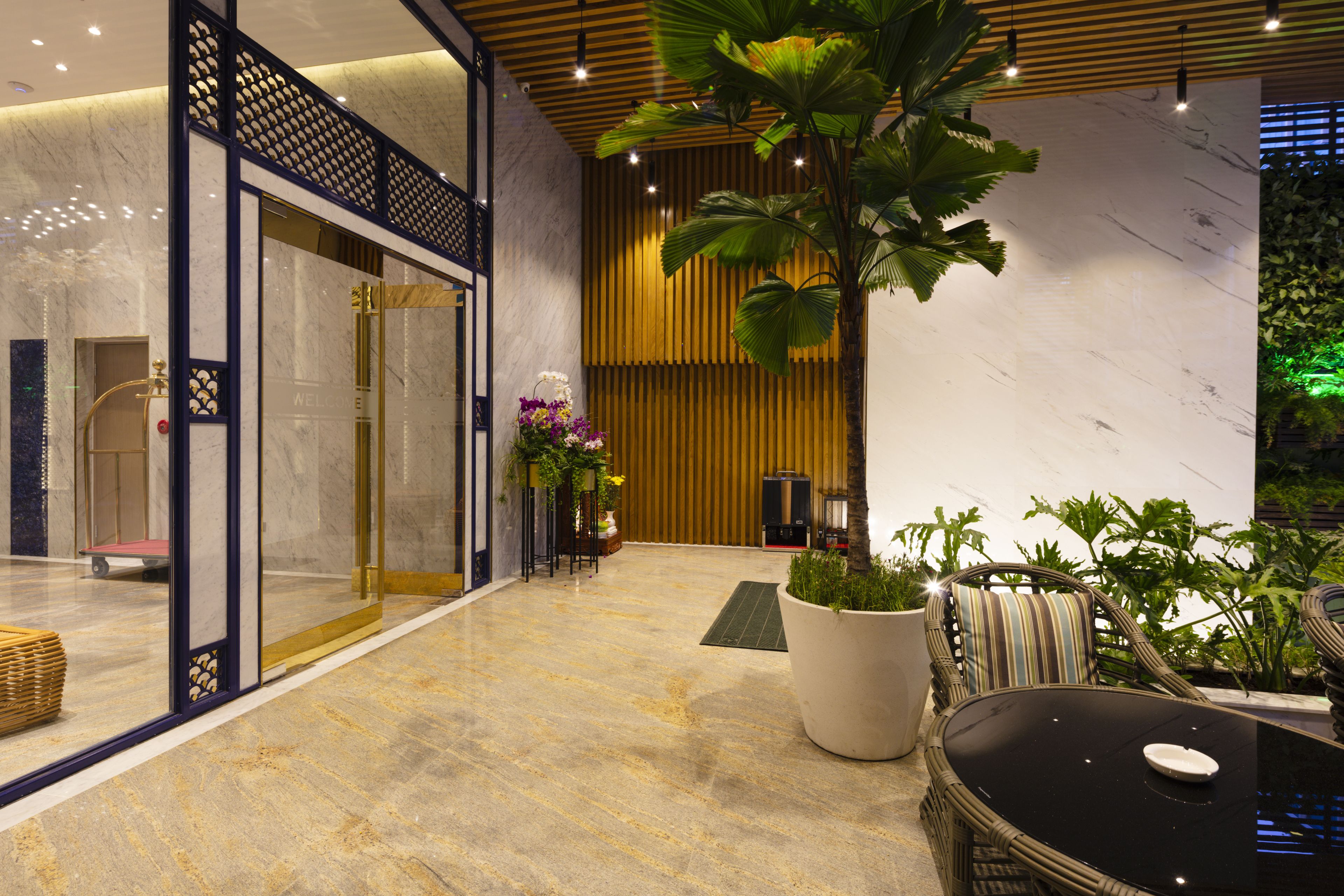 A lobby with a marble floor, a reception desk, a large potted plant, and a seating area with a table and chairs.