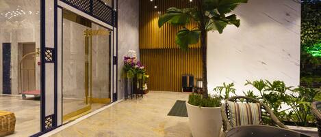 A lobby with a marble floor, a reception desk, a large potted plant, and a seating area with a table and chairs.