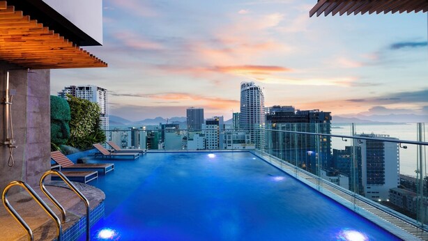 A rooftop infinity pool with a cityscape view, lounge chairs, and a glass railing. - Erica Nha Trang Hotel (Nha Trang)