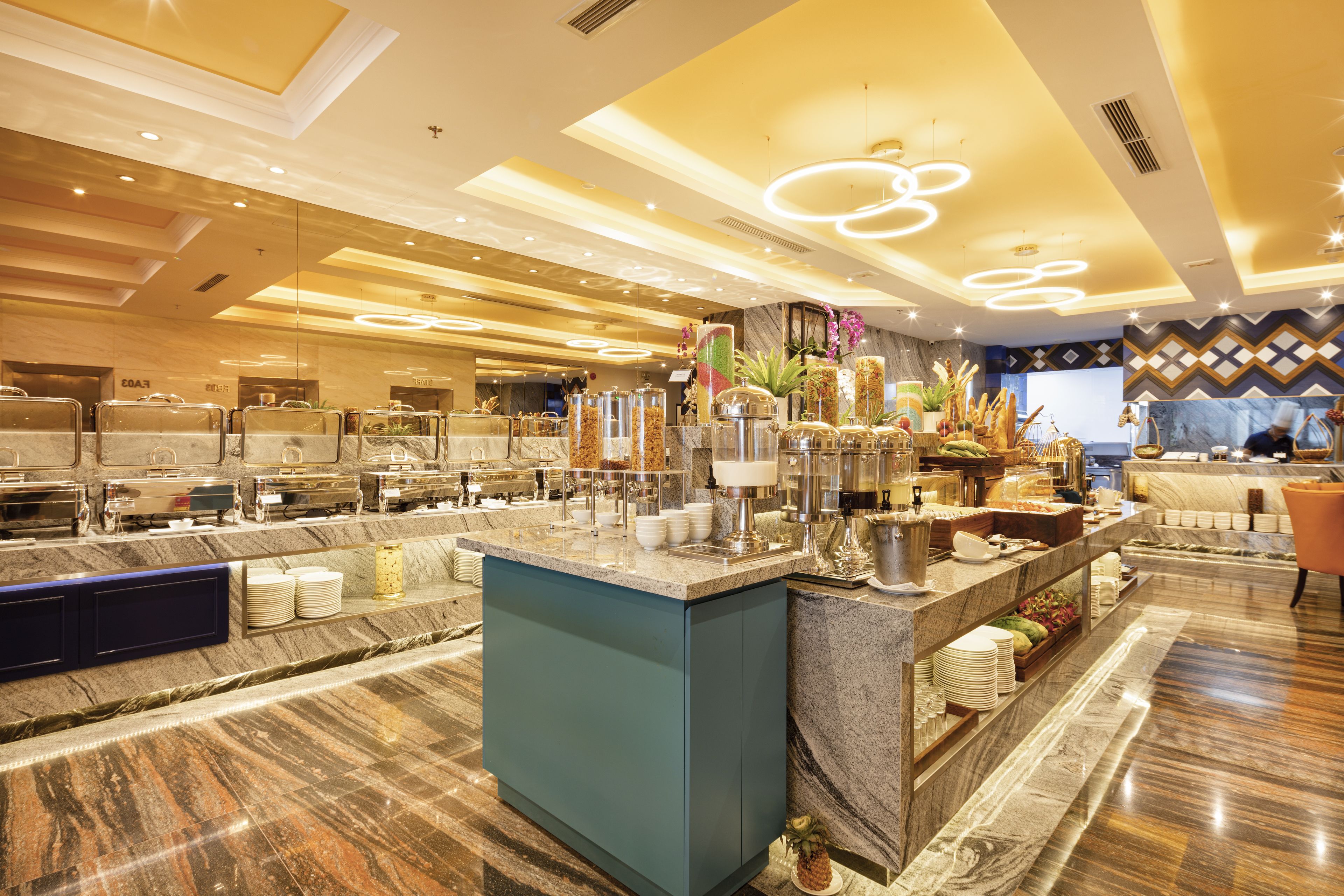 A modern hotel lobby with a marble reception desk, a buffet area, and a seating area with a patterned wall.
