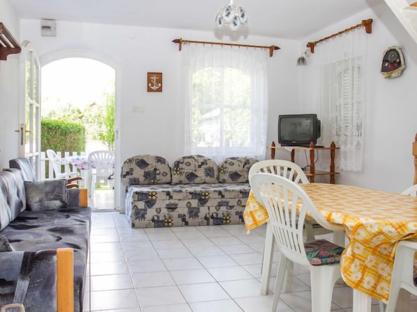 Un salon confortable avec un canapé, une table à manger et des chaises, un téléviseur et une fenêtre avec des rideaux.