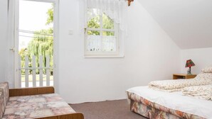 Une chambre à coucher avec un lit, une table de chevet, une fenêtre avec un rideau et une porte donnant sur l’extérieur.