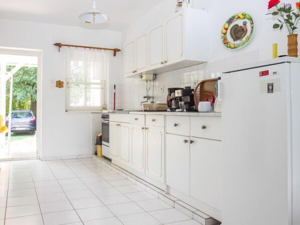 Una cocina con armarios blancos, un refrigerador y una ventana con cortina.
