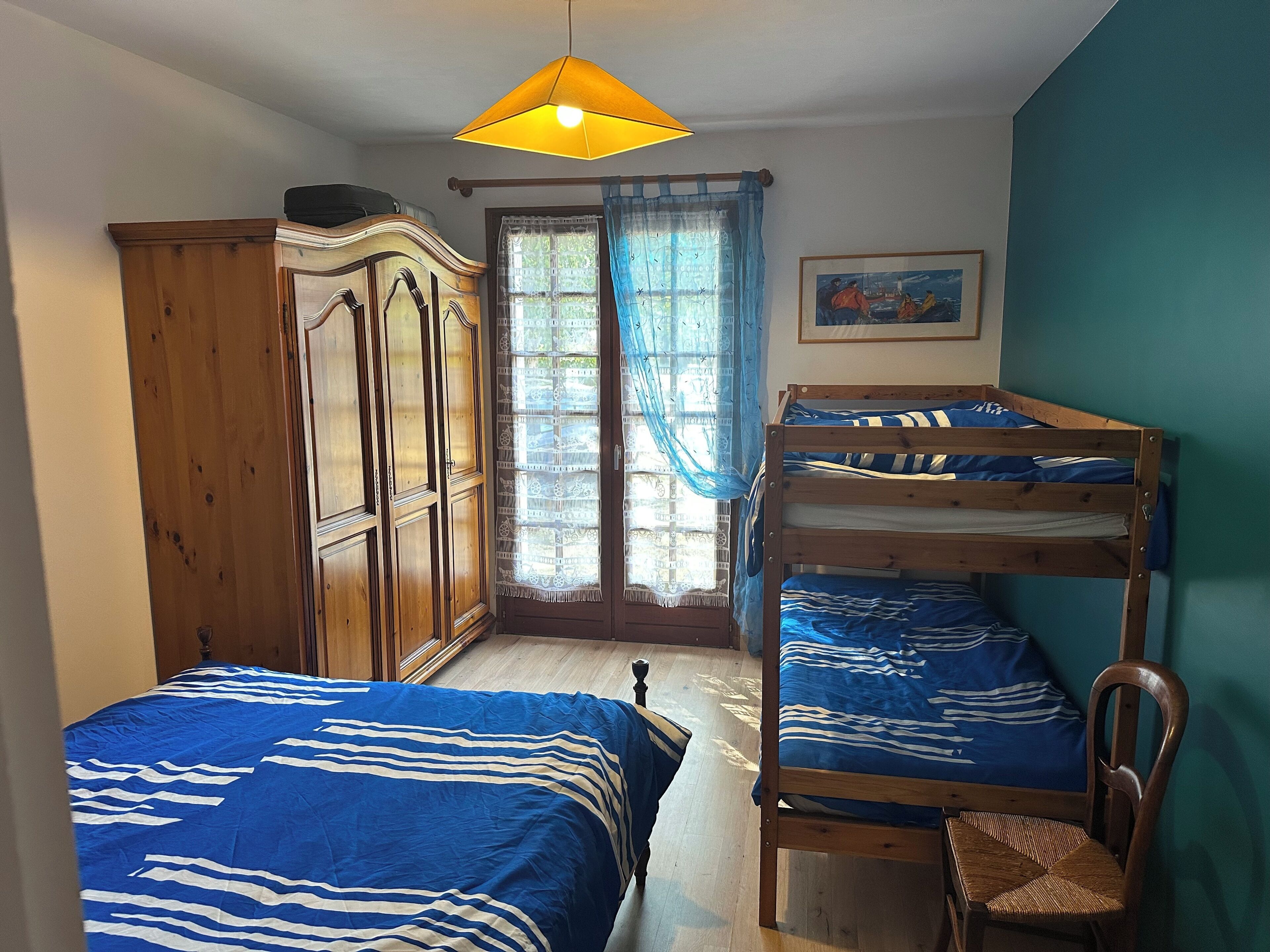 Une chambre avec un lit superposé, une armoire en bois, une chaise et une fenêtre avec des rideaux.