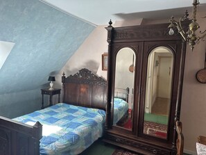 A bedroom with a large mirror, a bed with a blue and white patterned bedspread, a wooden nightstand with a lamp, and a chandelier. - House in Vannes (Gulf of Morbihan) (Séné)