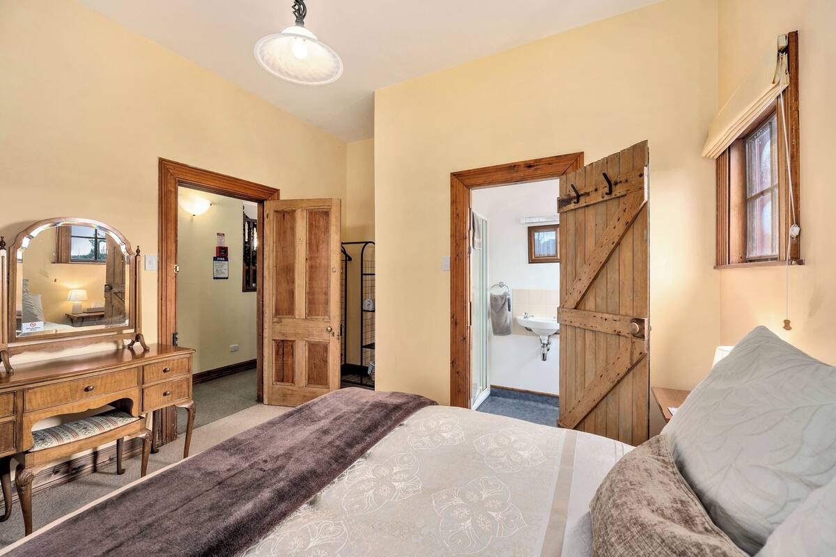 Een slaapkamer met een houten dressoir, een groot bed met een bedovertrek met dessin, en een badkamer met een houten deur.