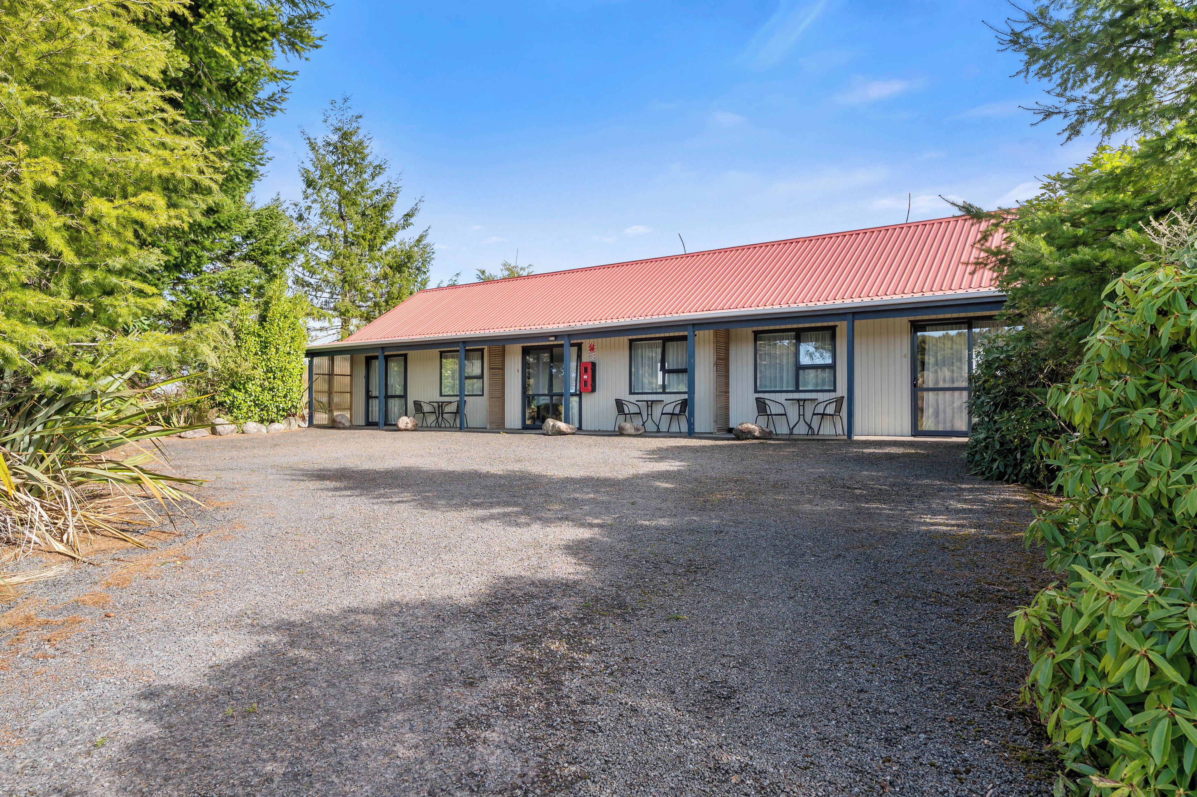 A motel with a red roof, a gravel driveway, and outdoor seating.