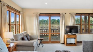 Une pièce spacieuse avec un grand lit, un canapé, un téléviseur posé sur un meuble en bois, et une vue sur l’extérieur grâce à de grandes fenêtres.