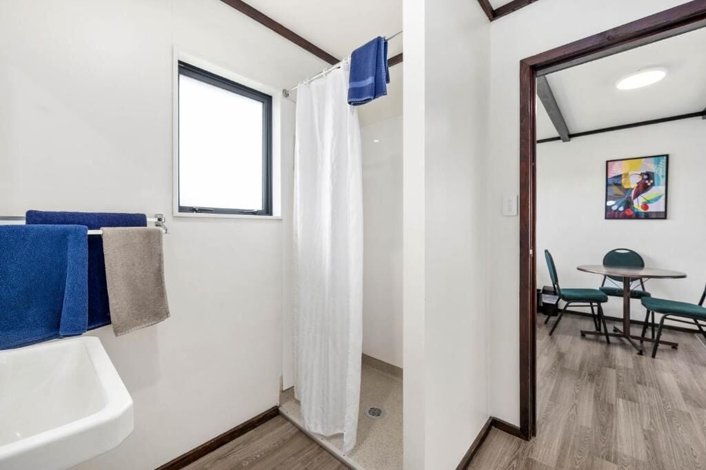 A bathroom with a sink, a shower curtain, and a window. There is a dining area with a table and chairs.