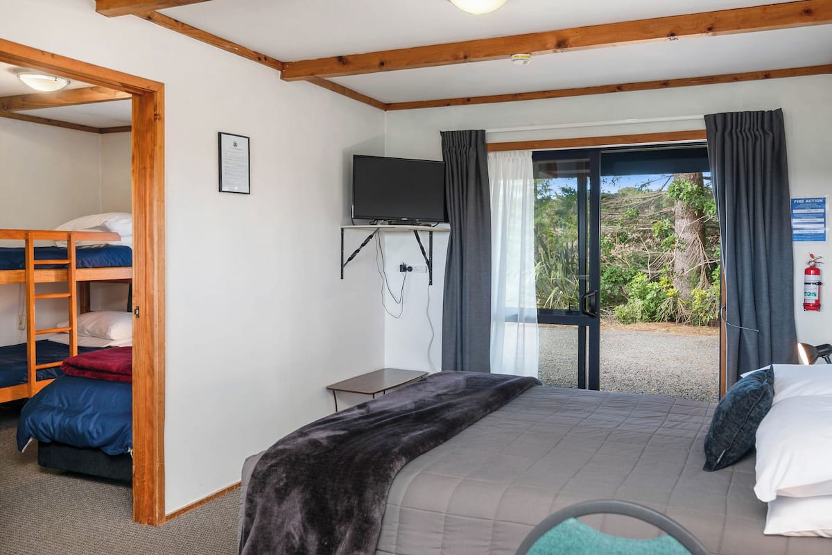 Een slaapkamer met een stapelbed, een flatscreen televisie aan de muur, een klein tafeltje en uitzicht op de omgeving via een glazen deur.