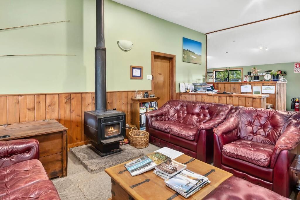 A cozy room with a wood-burning stove, leather sofas, a wooden coffee table with magazines, and a bookshelf.