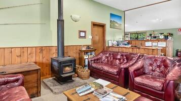 A cozy room with a wood-burning stove, leather sofas, a wooden coffee table with magazines, and a bookshelf.