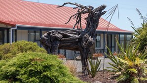 Une sculpture représentant un arbre, située dans un espace paysager, avec un bâtiment en arrière-plan.