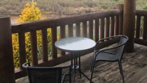 Une terrasse en bois avec une table et deux chaises, offrant une vue sur un paysage naturel composé de collines et d’arbres.
