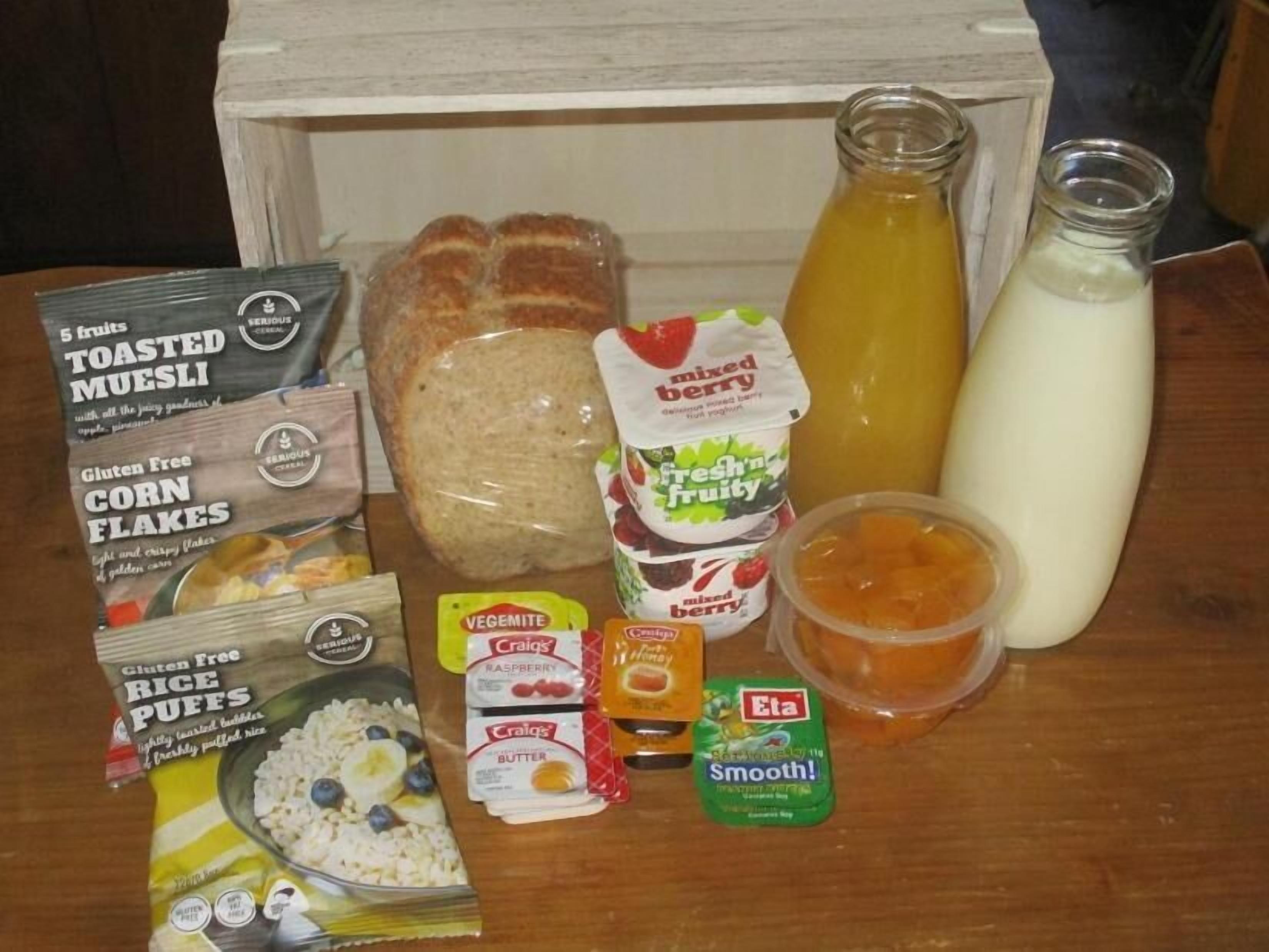 A variety of breakfast items including toasted muesli, corn flakes, rice puffs, mixed berry yogurt, and a bottle of orange juice.