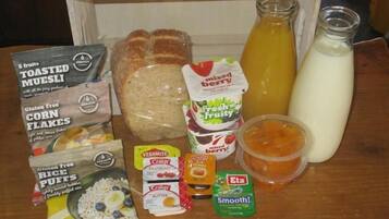 A variety of breakfast items including toasted muesli, corn flakes, rice puffs, mixed berry yogurt, and a bottle of orange juice.