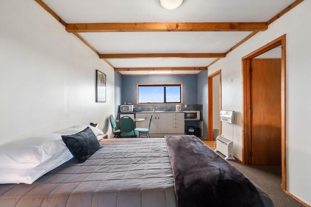 A bedroom with a bed, a desk, and a kitchenette.