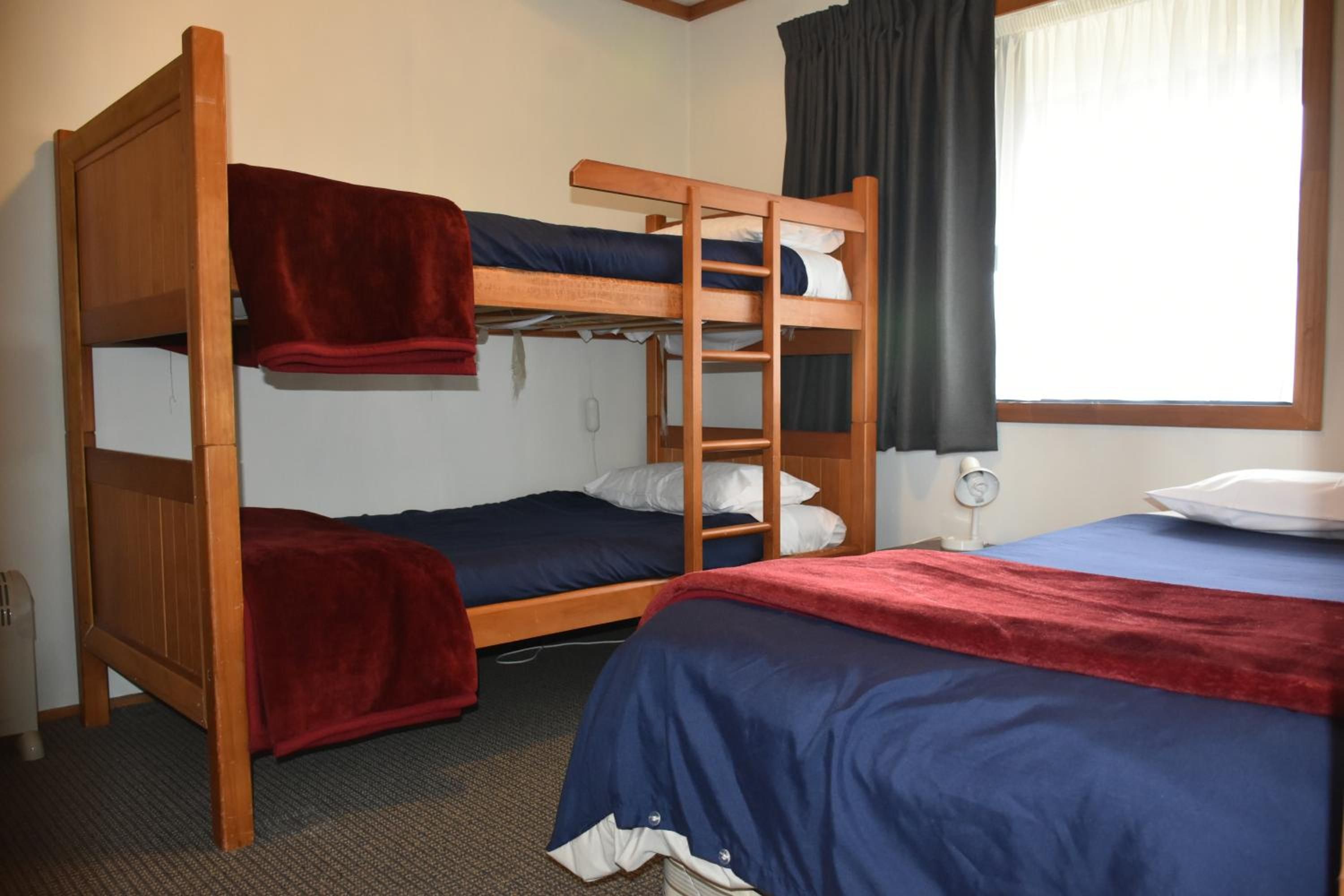 A bunk bed room with a red blanket on the lower bunk, a white pillow on the upper bunk, and a white lamp on the nightstand.