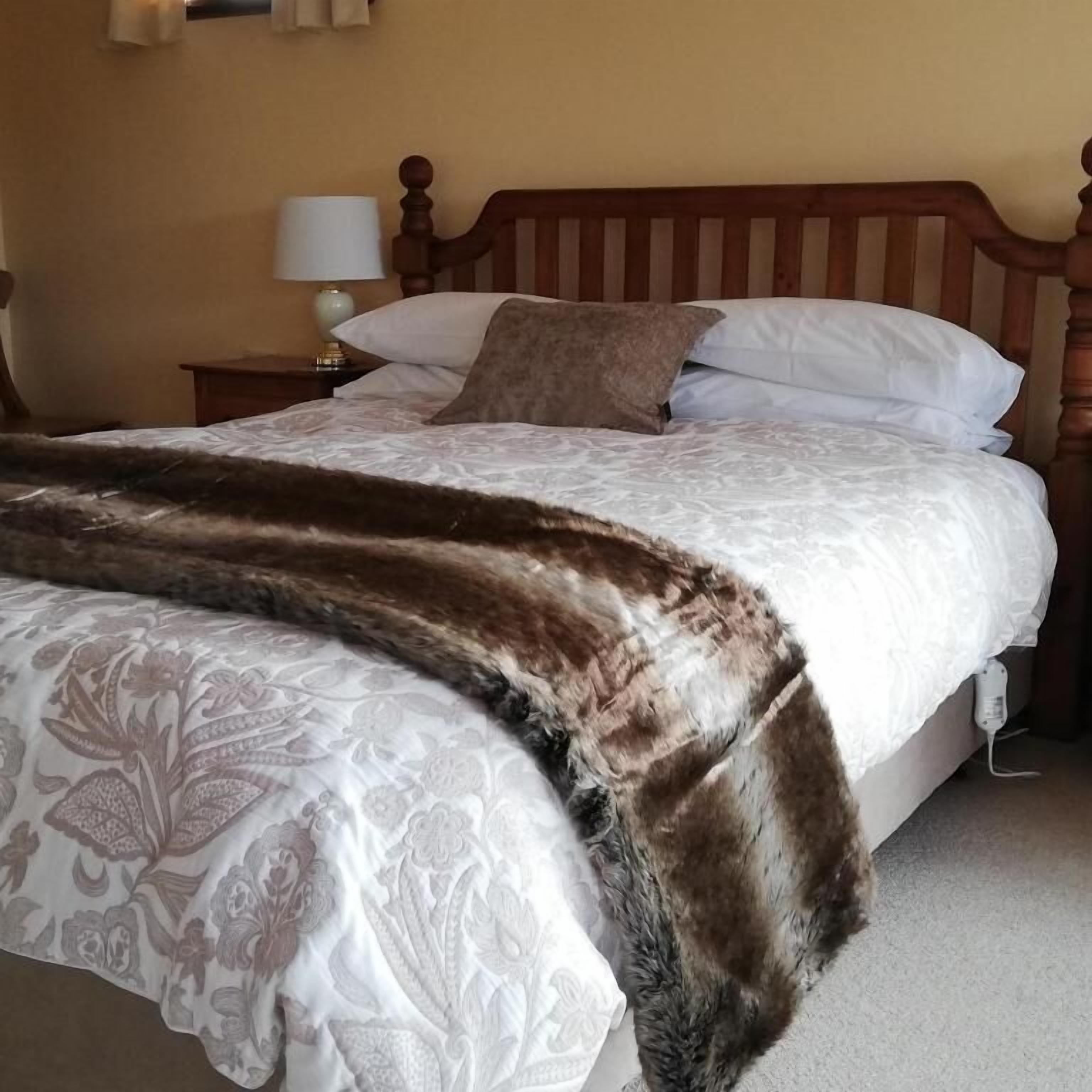 A bed with a patterned bedspread and a fur throw, a wooden headboard, and a bedside lamp.