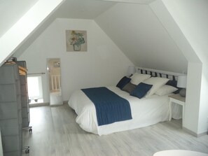 A bedroom with a sloped ceiling, a bed with white and blue bedding, a bedside table with a lamp, and a painting on the wall. - cottage in Créances village, 4 rooms, 4 people (Créances)