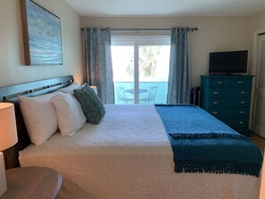 A hotel room with a bed, a TV, a dresser, and a balcony with a table and chairs.