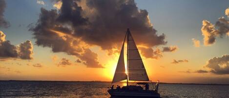 A sailboat on calm waters during sunset with a clear sky.