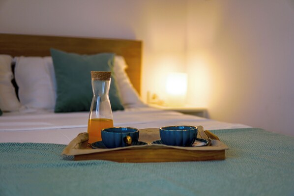 A tray with a glass bottle and two blue cups on a bed with a wooden headboard and pillows.