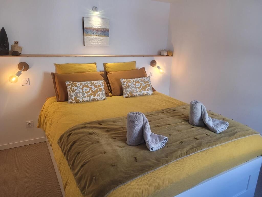 A neatly made bed with a yellow and brown bedspread, two pillows with floral patterns, and two folded towels on the bed.