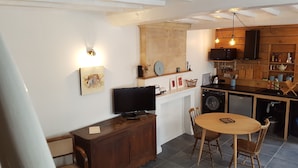 Un espacio habitable compacto con comedor, televisor, lavadora y cocina con estantes de madera.