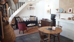 Una sala de estar acogedora con un sofá, una butaca roja y una mesa de comedor con sillas. Hay una chimenea, un televisor y una estantería llena de libros.