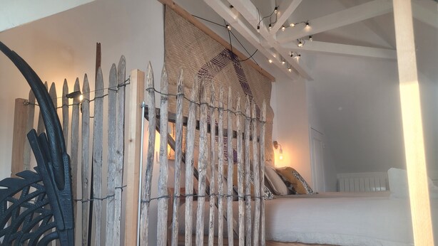 Un dormitorio con cama, una silla, un separador tejido y luces colgantes.