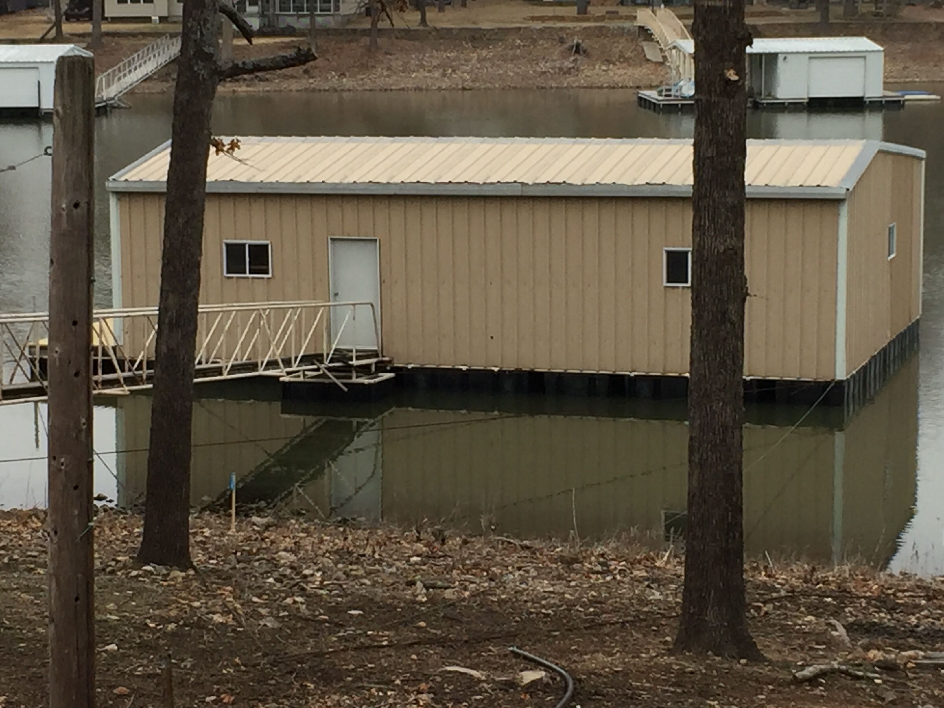 A single-story building with a flat roof, a door, and a small window, surrounded by trees and a body of water.