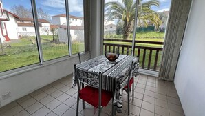 A balcony with a table and chairs, large windows with a view of houses and palm trees. - Cozy Ground Floor Studio, Terrace, Parking, Pet-Friendly - Cambo-les-Bains (Cambo-les-Bains)