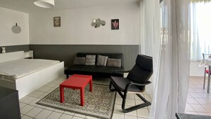 A modern living room with a sofa, a red table, a black chair, and a patterned rug. - Cozy Ground Floor Studio, Terrace, Parking, Pet-Friendly - Cambo-les-Bains (Cambo-les-Bains)