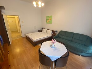 Ein Zimmer mit einem Bett, einem grünen Sofa, einem kleinen Tisch mit einer Vase und einer Tür zu einem anderen Raum.